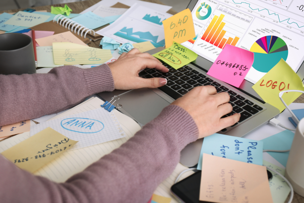 Desk with lots of post it notes and clutter, illustrating need for organization and a CRM system like 17hats.