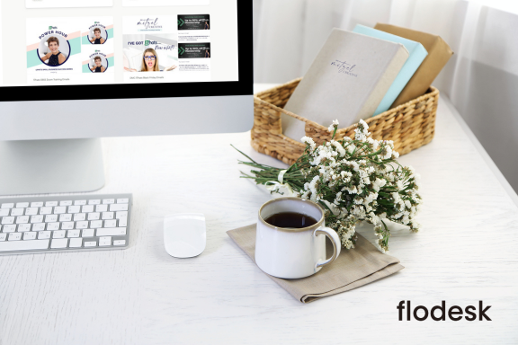 A white desktop workspace with an computer monitor, displaying Deb Mitzel Creative's Flodesk email templates. A basket of notebooks, a small bouquet of white flowers, and a cup of coffee sit beside a keyboard and mouse. The Flodesk logo appears in the bottom right corner.